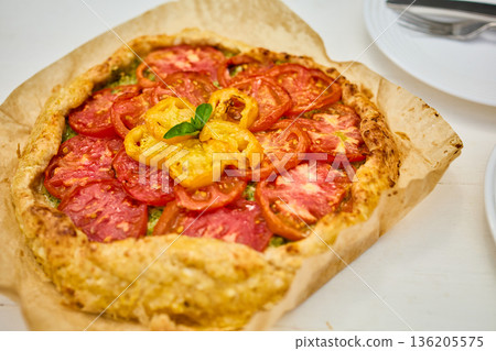 Freshly baked tomato galette on parchment paper served on a rustic wooden table in a cozy kitchen setting Freshly baked tomato galette on parchment paper served on a rustic wooden table in a cozy kitchen setting 136205575