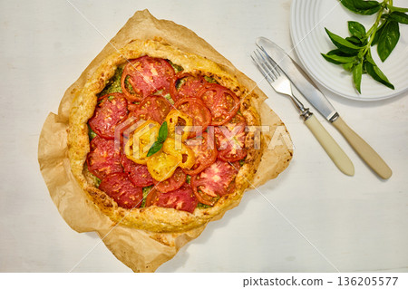 Freshly baked tomato galette on parchment paper served on a rustic wooden table in a cozy kitchen setting Freshly baked tomato galette on parchment paper served on a rustic wooden table in a cozy kitchen setting 136205577
