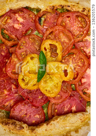 Freshly baked tomato galette on parchment paper served on a rustic wooden table in a cozy kitchen setting Freshly baked tomato galette on parchment paper served on a rustic wooden table in a cozy kitchen setting 136205579