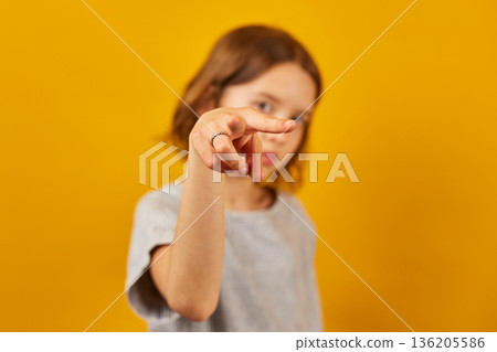Child making a finger-pointing gesture against a bright yellow background during a playful moment Child making a finger-pointing gesture against a bright yellow background during a playful moment 136205586