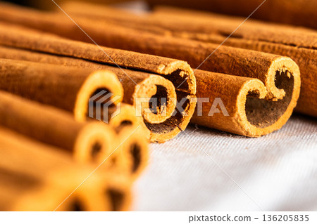 Cinnamon cassia sticks stacked together, showcasing their rich brown color and curled ends. Ideal for culinary and aromatic uses. 136205835