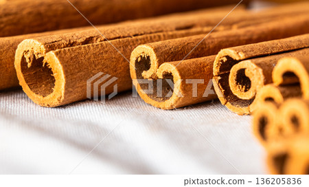 Cinnamon cassia sticks stacked together, showcasing their rich brown color and curled ends. Ideal for culinary and aromatic uses. 136205836