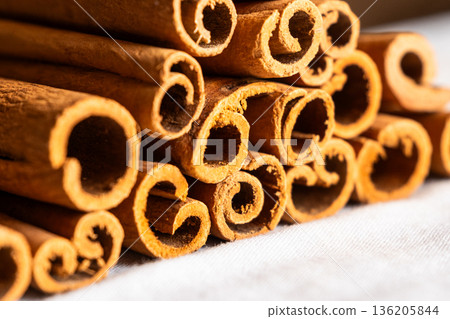 Cinnamon cassia sticks stacked together, showcasing their rich brown color and curled ends. Ideal for culinary and aromatic uses. 136205844
