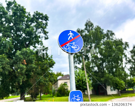 Shared pedestrian and bicycle path with traffic signs crossed with red line. Urban settings against green trees and blue sky 136206374