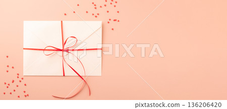 White envelope with red ribbon and sequin heart on pastel background White envelope with red ribbon and sequin heart on pastel background 136206420
