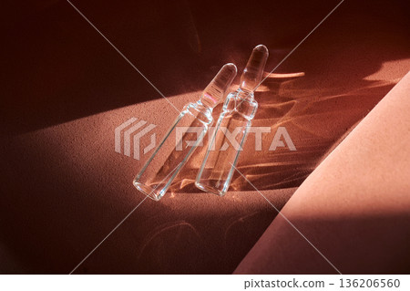 Two glass ampoules showcasing light refraction on textured surface 136206560