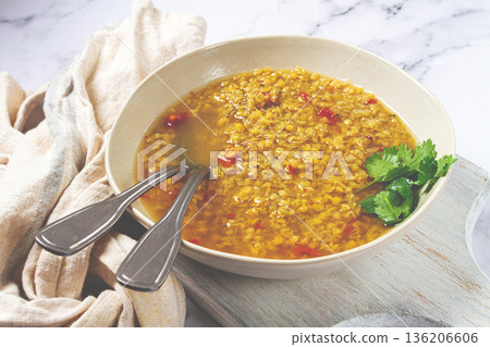 Delicious lentil soup served in a bowl on a rustic surface with garnishes and utensils Delicious lentil soup served in a bowl on a rustic surface with garnishes and utensils 136206606