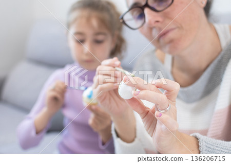 Mother and daughter painting Easter eggs at home. Mother and daughter painting Easter eggs at home. 136206715