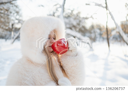 Young woman drinking hot drink in winter park 136206737