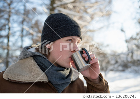 Man drinking hot beverage outdoors in snowy winter park 136206745