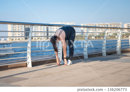 Pregnant Woman Stretching By The Water On A Sunny Day In Sleek Active wear. Pregnant Woman Stretching By The Water On A Sunny Day In Sleek Active wear. 136206773