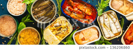 A top view of open tin cans with canned salmon, mackerel, sprat, sardine, tuna, herring, and fish pate, surrounded by spices and herbs on a blue background, banner A top view of open tin cans with canned salmon, mackerel, sprat, sardine, tuna, herring, and fish pate, surrounded by spices and herbs on a blue background, banner 136206860