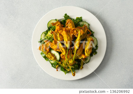 Roasted zucchini flowers sit on a bed of salad made with fresh greens, cucumbers, and broccoli. This dish highlights summer flavors and healthy eating options 136206992