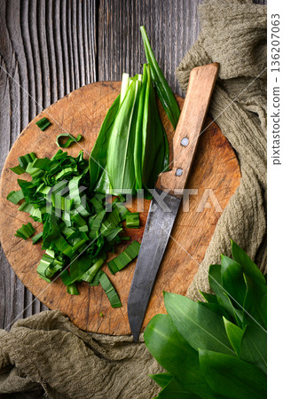 Chopping fresh wild garlic leaves on round wooden cutting board Chopping fresh wild garlic leaves on round wooden cutting board 136207063