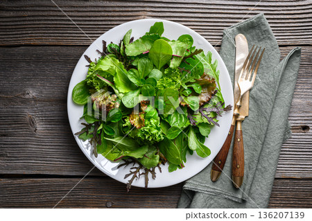 Fresh mixed salad greens on white plate on wooden table Fresh mixed salad greens on white plate on wooden table 136207139