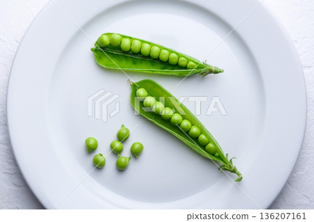 Green peas with open pods on a white plate from above 136207161