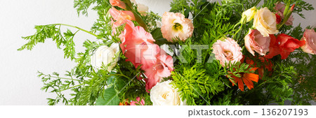 A bouquet of roses, gladioli, zinnias, and eustomas stands in water. Carrots with green tops are part of the arrangement on a plain table against a light background, banner 136207193