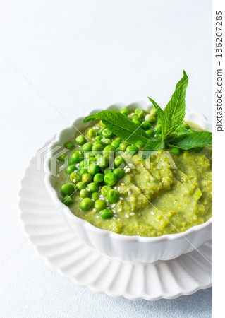 A bowl of vibrant green pea and broccoli soup is topped with fresh mint leaves for flavor. This healthy dish is perfect for a warm lunch or cozy dinner at home A bowl of vibrant green pea and broccoli soup is topped with fresh mint leaves for flavor. This healthy dish is perfect for a warm lunch or cozy dinner at home 136207285
