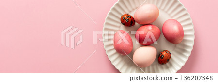A collection of beautifully dyed Easter eggs in various shades rests on a decorative plate, set against a soft pink background, celebrating the joyful holiday spirit, banner A collection of beautifully dyed Easter eggs in various shades rests on a decorative plate, set against a soft pink background, celebrating the joyful holiday spirit, banner 136207348