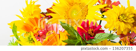 A bouquet featuring sunflowers and zinnias sits in a vase against a plain background. The flowers are vibrant and colorful, showing a mix of yellow, orange, and pink hues, banner 136207355