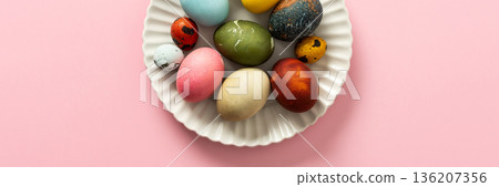 A collection of vibrant Easter eggs in various colors is artfully arranged on a white plate, set against a soft pink background, capturing the essence of the holiday's decorations, banner A collection of vibrant Easter eggs in various colors is artfully arranged on a white plate, set against a soft pink background, capturing the essence of the holiday's decorations, banner 136207356