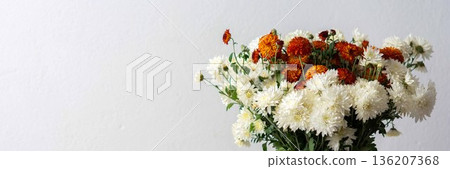 A white pitcher filled with orange and white flowers sits on a light surface. This setup can be used for home decoration or floral arrangement inspiration, banner A white pitcher filled with orange and white flowers sits on a light surface. This setup can be used for home decoration or floral arrangement inspiration, banner 136207368