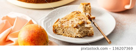 A slice of pear pie sits on a white plate with a fork. A warm coffee cup is next to it. Fresh pears are placed on the table, adding to the scene, banner 136207369