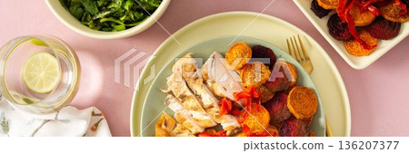 Baked potato is served with chicken breast and roasted carrots, peppers, and beets on a plate. A light meal is arranged on a simple table setting, banner Baked potato is served with chicken breast and roasted carrots, peppers, and beets on a plate. A light meal is arranged on a simple table setting, banner 136207377