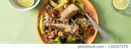 Breakfast includes baked hake placed on boiled beans with broccoli and peppers. A fresh tomato salad and lime water are nearby on a green table, banner Breakfast includes baked hake placed on boiled beans with broccoli and peppers. A fresh tomato salad and lime water are nearby on a green table, banner 136207379