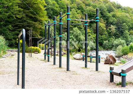 Outdoor fitness playground with pull-up bars near river and forest. Street workout equipment in natural environment, Sports equipment for bodyweight training, gymnastics, and healthy outdoor activity Outdoor fitness playground with pull-up bars near river and forest. Street workout equipment in natural environment, Sports equipment for bodyweight training, gymnastics, and healthy outdoor activity 136207537