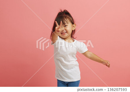 happy little asian girl cheerful showing V gesture standing over pink isolated background. happy little asian girl cheerful showing V gesture standing over pink isolated background. 136207593
