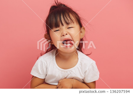 Stubborn three year old Asian little girl capriciously shows her tongue to the camera on a pink isolated background. Naughty child concept Stubborn three year old Asian little girl capriciously shows her tongue to the camera on a pink isolated background. Naughty child concept 136207594