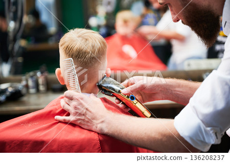 Barber using comb and shaver to cut hair. Professional hairdresser shaving little kid's nape. Close up. 136208237