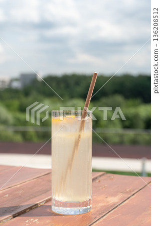 Tall glass of citrus lemonade with ice and bamboo straw on wooden table with green park background. Refreshing summer drink Tall glass of citrus lemonade with ice and bamboo straw on wooden table with green park background. Refreshing summer drink 136208512