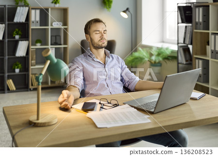Man meditating at laptop during remote work break in modern home office interior 136208523