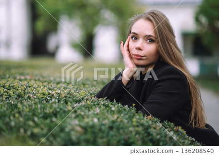 Thoughtful Young Woman Portrait Outdoors Leaning on Green Hedge in Urban Park with Soft Natural Light and Calm Elegant Mood Thoughtful Young Woman Portrait Outdoors Leaning on Green Hedge in Urban Park with Soft Natural Light and Calm Elegant Mood 136208540