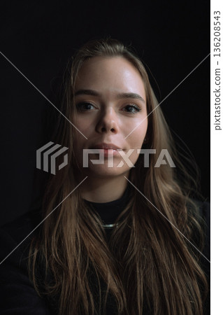 Dark Cinematic Front Facing Portrait of Young Woman with Natural Skin Texture Soft Directional Light and Deep Black Background Creating Calm Emotional Presence 136208543