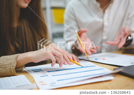 Two people reviewing financial data discussing performance results and analyzing business strategy Two people reviewing financial data discussing performance results and analyzing business strategy 136208641