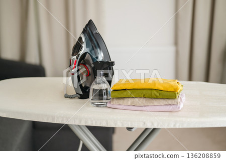 Ironing clothes. Electric iron over ironing board at home with pile of shirts. Daily chores. Laundry day. 136208859