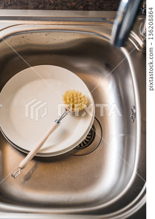 Authentic sustainability concept. Wooden brush for washing dishes in the kitchen sink. Eco friendly, zero waste or conscious consumption concept. Authentic sustainability concept. Wooden brush for washing dishes in the kitchen sink. Eco friendly, zero waste or conscious consumption concept. 136208864