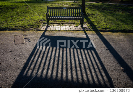 Park bench casting a long shadow in the late afternoon light Park bench casting a long shadow in the late afternoon light 136208973