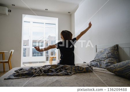 Woman stretching arms after waking up in bedroom Woman stretching arms after waking up in bedroom 136209488