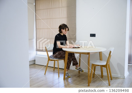 Woman reading book at table in modern kitchen Woman reading book at table in modern kitchen 136209498