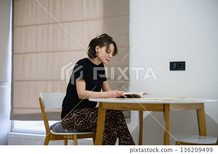 Woman reading book at table in modern kitchen 136209499