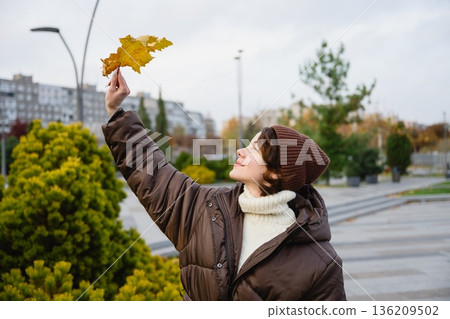 Woman holding autumn leaf in city park 136209502