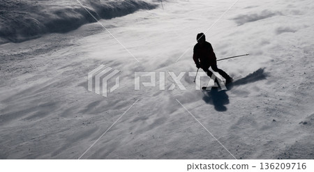 A skier glides down a snowy slope in Bad Gastein. The snow is fresh, and the weather is cold. This scene captures the excitement of winter sports in the mountains. 136209716