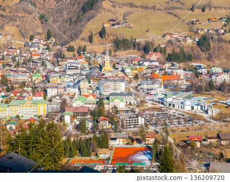Bad Gastein village from a high viewpoint. Buildings of various styles are nestled in the valley surrounded by mountains and greenery. People visit this area for recreation. Bad Gastein village from a high viewpoint. Buildings of various styles are nestled in the valley surrounded by mountains and greenery. People visit this area for recreation. 136209720