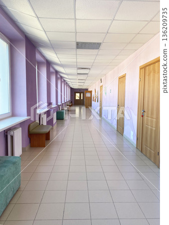 Bright corridor with purple walls and large windows, featuring benches and doors, creating a spacious and inviting atmosphere for visitors and residents in a modern building 136209735
