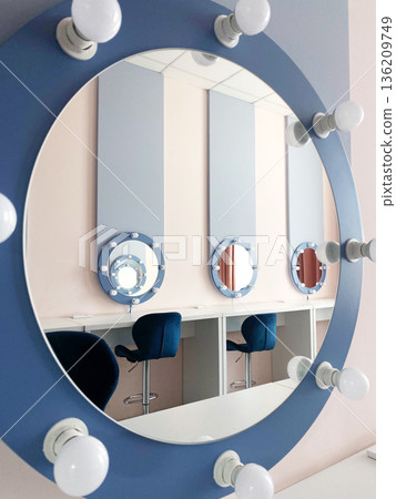 Circular mirror with bright bulbs reflects modern vanity area featuring blue chairs and pastel walls, creating a stylish and inviting atmosphere for beauty routines Circular mirror with bright bulbs reflects modern vanity area featuring blue chairs and pastel walls, creating a stylish and inviting atmosphere for beauty routines 136209749