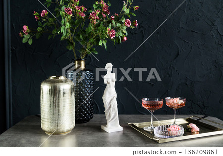 Elegant still life arrangement featuring a decorative vase, a classic sculpture, and stylish glassware with floral accents, creating a sophisticated ambiance for interior decor Elegant still life arrangement featuring a decorative vase, a classic sculpture, and stylish glassware with floral accents, creating a sophisticated ambiance for interior decor 136209861
